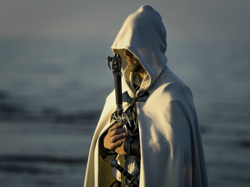 Portrait of assassin in white costume with the sword at the sea.